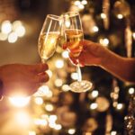 Couple holding glasses of champagne in front of Christmas tree. Toasting to each other. Evening or night.